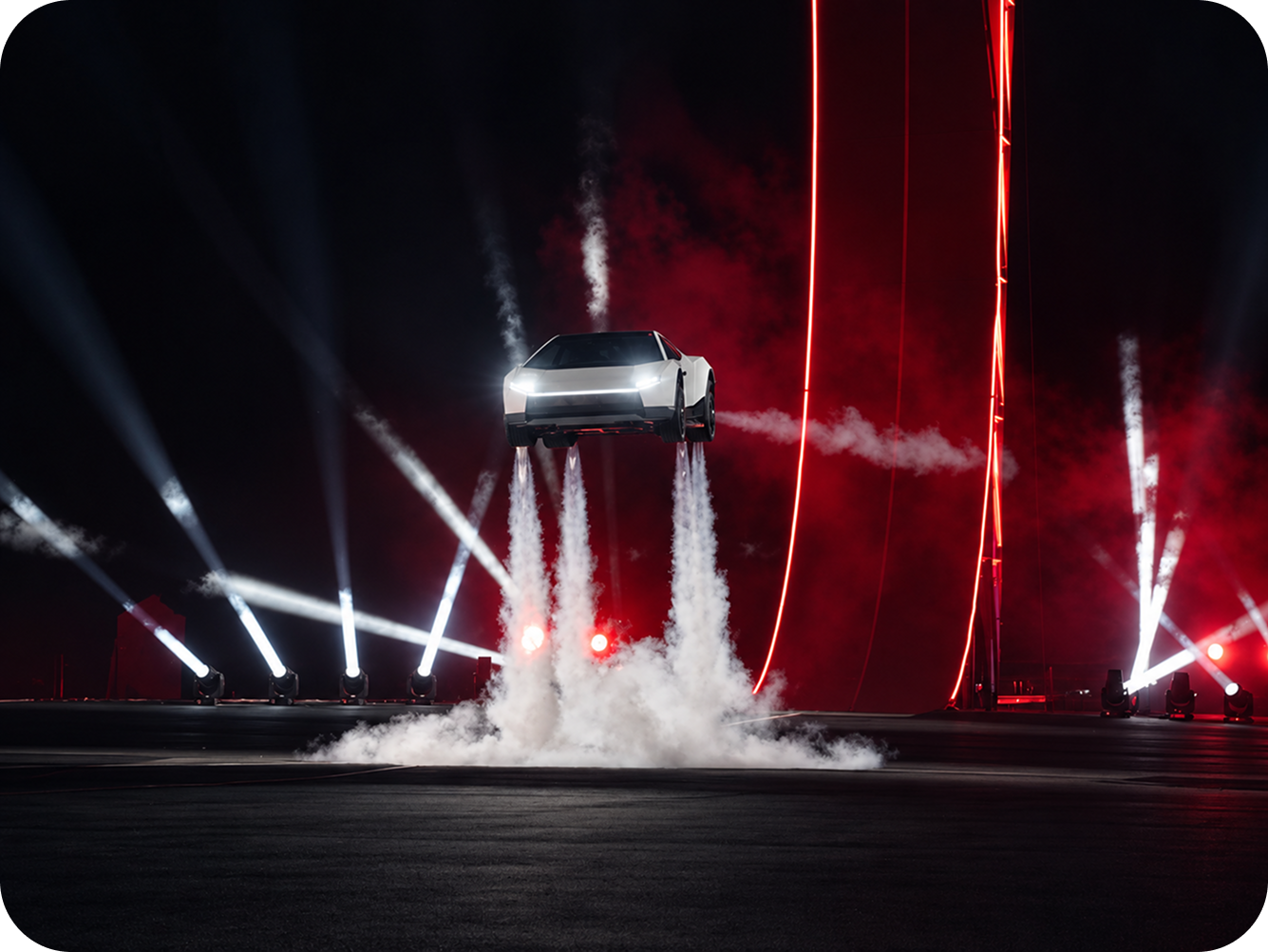 Tesla Roadster branco suspenso no ar durante apresentação futurista, com jatos de fumaça, iluminação vermelha e holofotes, representando o conceito de carro esportivo voador.