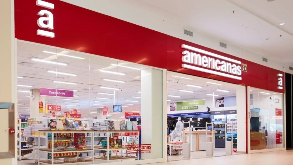 Fachada de uma loja Americanas em shopping, com logotipo vermelho e branco e prateleiras de produtos, ilustrando o encerramento da recuperação judicial em 2026.